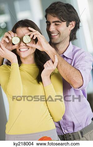 Man holding cucumber slices in front of a woman in the kitchen View Large Photo Image Picture - Man holding cucumber slices in front of a woman in the kitchen. Fotosearch