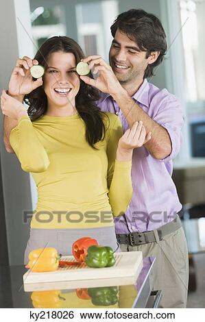Man holding cucumber slices in front of a woman in the kitchen View Large Photo Image Stock Photograph - Man holding cucumber slices in front of a woman in the kitchen. Fotosearch