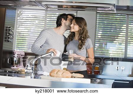 Stock Image - Man kissing a woman in the kitchen. Fotosearch