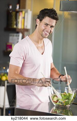 Picture - Man mixing vegetable salad in the kitchen. Fotosearch