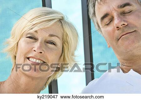 Stock Photo - Portrait of a woman smiling beside a man sleeping. Fotosearch