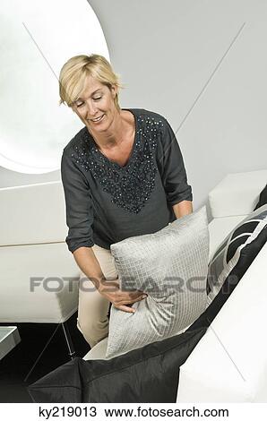 Woman arranging cushions on a couch and smiling View Large Photo Image Stock Image - Woman arranging cushions on a couch and smiling. Fotosearch