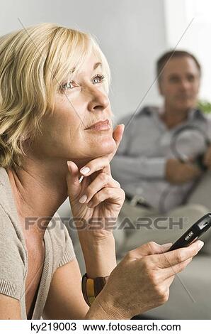 Stock Image - Woman holding a mobile phone and thinking. Fotosearch