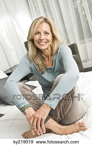 Woman sitting on the bed and smiling View Large Photo Image Stock Photo - Woman sitting on the bed and smiling. Fotosearch