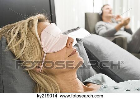 Picture - Woman wearing an eye mask and her husband listening to music in the background. Fotosearch