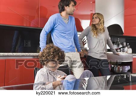 Boy playing a video game with his parents in the background View Large Photo Image Stock Image - Boy playing a video game with his parents in the background. Fotosearch