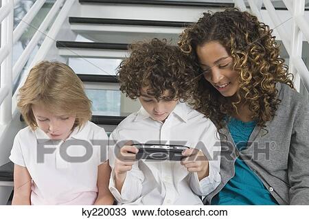 Boy playing a video game with his sisters View Large Photo Image Stock Image - Boy playing a video game with his sisters. Fotosearch