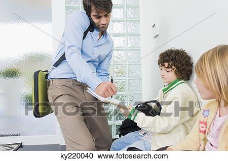 Stock Image - Man signing his son's notebook and talking on a mobile phone. Fotosearch
