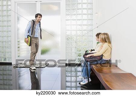 Stock Image - Man walking towards his children waiting in an entrance hall. Fotosearch