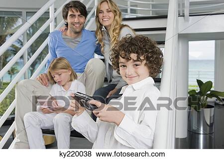 Stock Photo - Parents sitting on steps with their children playing video games. Fotosearch