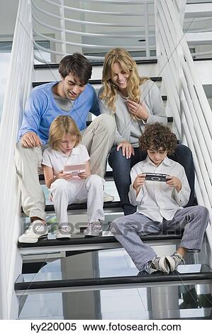 Parents sitting on steps with their children playing video games View Large Photo Image Stock Photography - Parents sitting on steps with their children playing video games. Fotosearch