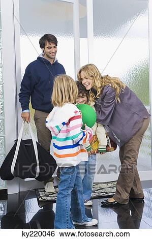 Stock Photograph - Woman greeting her children and husband at the door of a house. Fotosearch