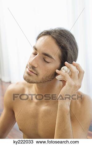 Man holding a conch shell to ear View Large Photo Image Stock Image - Man holding a conch shell to ear. Fotosearch