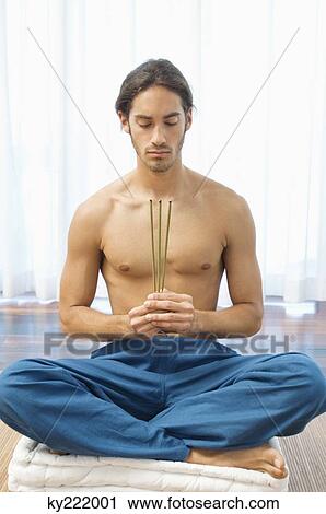 Stock Image - Man practicing yoga and holding incense sticks. Fotosearch