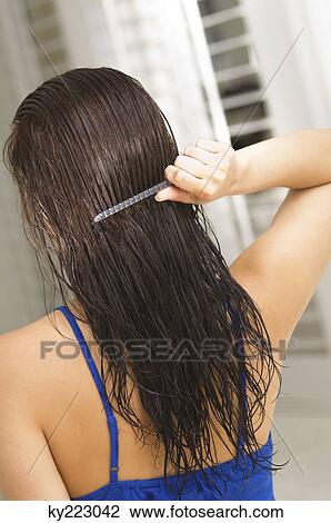 Stock Image - Rear view of a woman combing her hair. Fotosearch