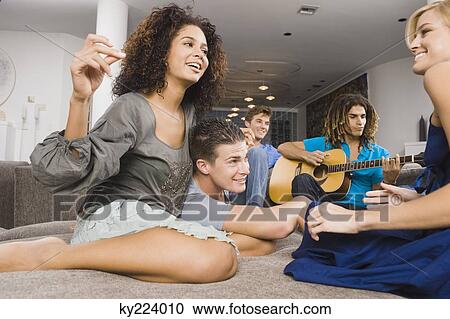 Stock Image - Man sitting with his friends and playing a guitar. Fotosearch