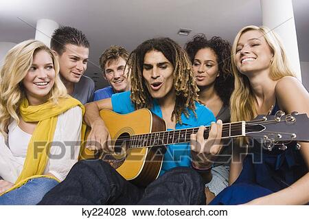 Stock Photo - Man sitting with his friends and playing a guitar. Fotosearch