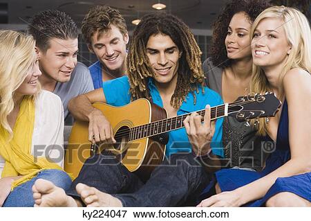 Man sitting with his friends and playing a guitar View Large Photo Image Stock Photo - Man sitting with his friends and playing a guitar. Fotosearch