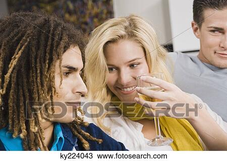 Stock Image - Woman holding a glass of wine and sitting with her friends. Fotosearch