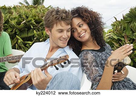 Stock Image - Woman playing a drum with her friends playing guitars. Fotosearch