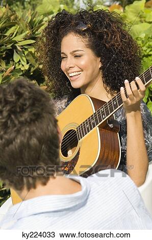 Woman playing a guitar in front of a man View Large Photo Image Stock Image - Woman playing a guitar in front of a man. Fotosearch