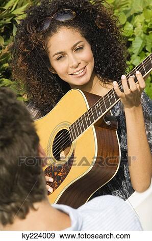 Stock Photo - Woman playing a guitar in front of a man. Fotosearch