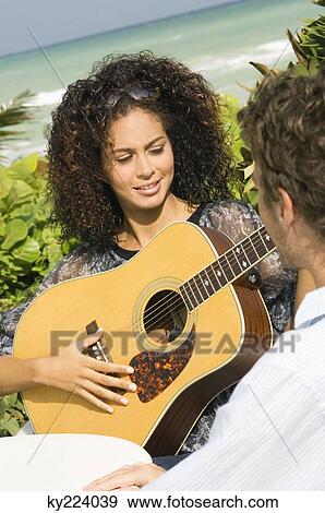 Woman playing a guitar in front of a man View Large Photo Image Stock Photo - Woman playing a guitar in front of a man. Fotosearch