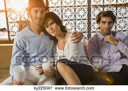 Stock Photo - Portrait of a couple sitting with their friend. Fotosearch