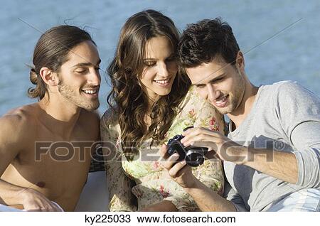 Stock Image - Three friends looking at a digital camera. Fotosearch