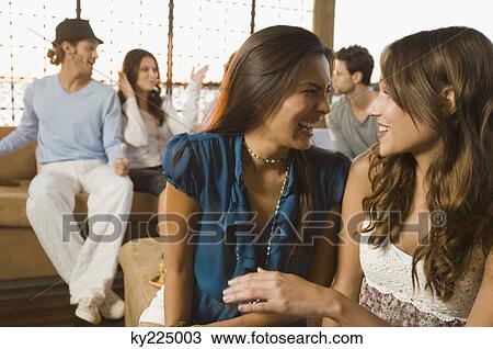 Stock Image - Two women smiling with their friends in the background. Fotosearch