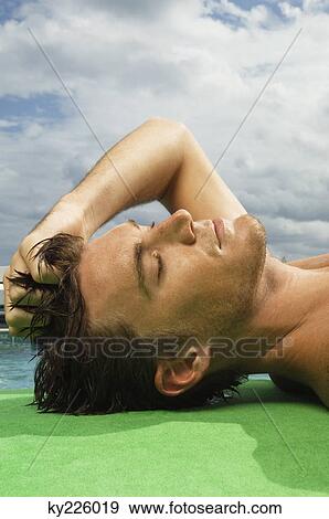 Man sunbathing at the poolside View Large Photo Image Stock Photo - Man sunbathing at the poolside. Fotosearch