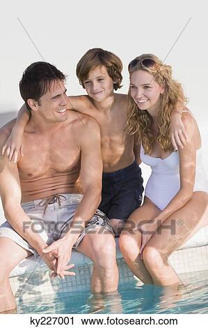 Stock Image - Family sitting at the poolside and smiling. Fotosearch