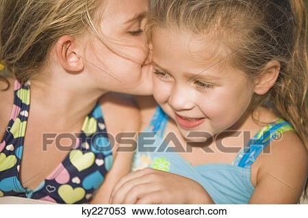 Stock Image - Girl whispering into her friend's ear. Fotosearch