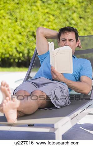 Stock Photograph - Man reading a book on a lounge chair. Fotosearch