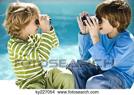 Picture - Two boys looking at each other through binoculars at the poolside. Fotosearch