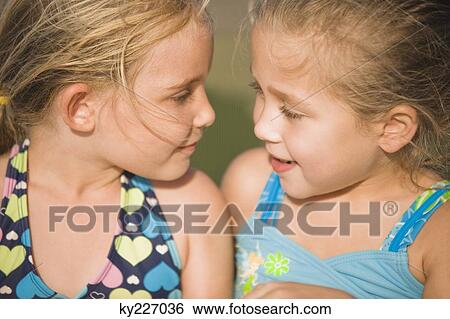 Two girls looking at each other and smiling View Large Photo Image Stock Photograph - Two girls looking at each other and smiling. Fotosearch