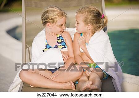 Picture - Two girls sitting on a lounge chair at the poolside. Fotosearch