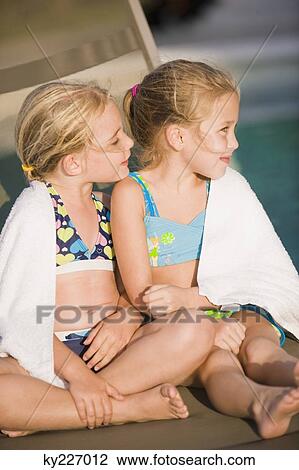 Stock Image - Two girls sitting on a lounge chair at the poolside. Fotosearch