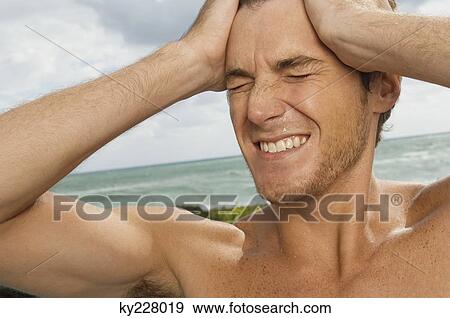 Man holding his head in pain on the beach View Large Photo Image Stock Photo - Man holding his head in pain on the beach. Fotosearch
