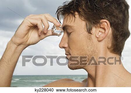 Man rubbing an ice cube on his forehead View Large Photo Image Stock Image - Man rubbing an ice cube on his forehead. Fotosearch