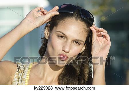 Portrait of a woman adjusting sunglasses and puckering her lips View Large Photo Image Stock Photo - Portrait of a woman adjusting sunglasses and puckering her lips. Fotosearch