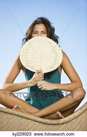 Stock Image - Woman holding a hand fan in front of her mouth. Fotosearch
