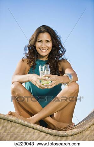 Woman sitting on a chaise longue and holding a glass of lemonade View Large Photo Image Stock Image - Woman sitting on a chaise longue and holding a glass of lemonade. Fotosearch