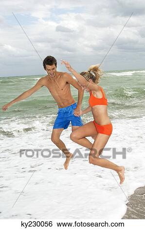 Couple holding hands and jumping on the beach View Large Photo Image Stock Photograph - Couple holding hands and jumping on the beach. Fotosearch