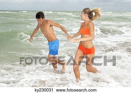 Couple running in water on the beach View Large Photo Image Stock Image - Couple running in water on the beach. Fotosearch