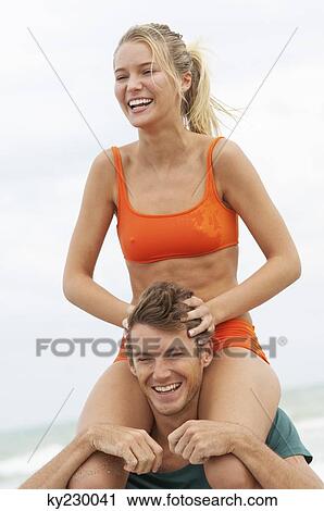 Stock Image - Man carrying a woman on his shoulders on the beach. Fotosearch