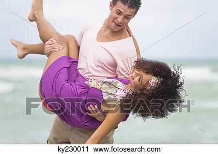 Man carrying a woman on the beach View Large Photo Image Stock Image - Man carrying a woman on the beach. Fotosearch