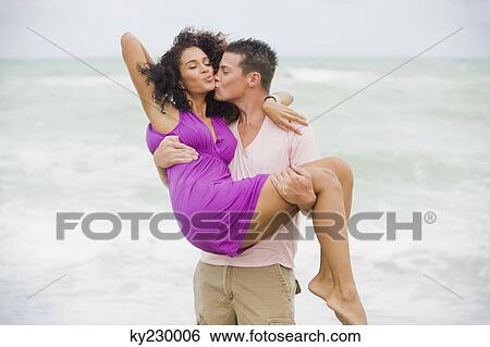 Man carrying and kissing a woman on the beach View Large Photo Image Stock Photograph - Man carrying and kissing a woman on the beach. Fotosearch