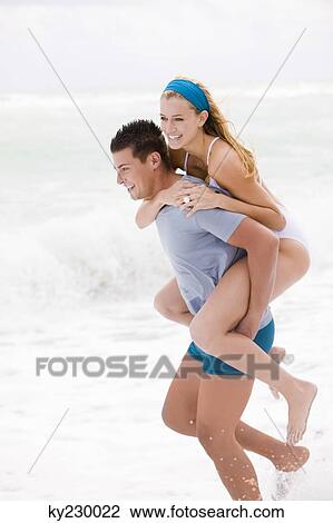Man giving woman piggyback ride on the beach View Large Photo Image Stock Image - Man giving woman piggyback ride on the beach. Fotosearch