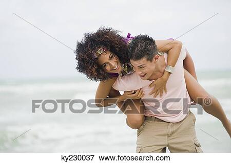 Man giving woman piggyback ride on the beach View Large Photo Image Stock Photo - Man giving woman piggyback ride on the beach. Fotosearch